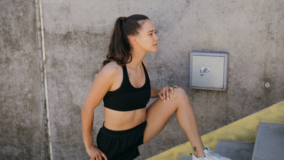 Woman in athletic wear stretching outdoors on steps, embodying wellness and fitness.